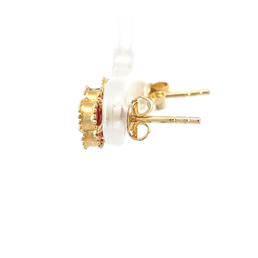 Close-up of red-accented gold earrings under soft lighting